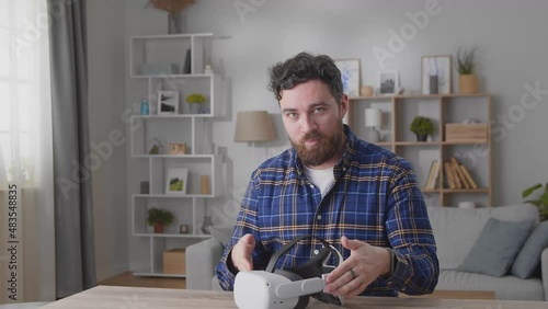 Young man sitting at desk and talking to camera while recording video blog about virtual reality technology