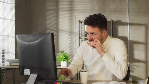 Busy casual young businessman eating lunch sandwich food at office desk writing