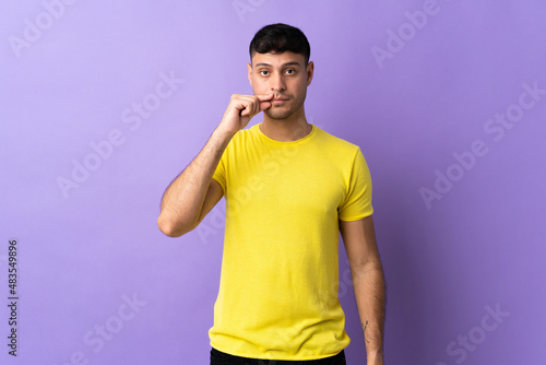 Young Colombian man isolated on purple background showing a sign of silence gesture