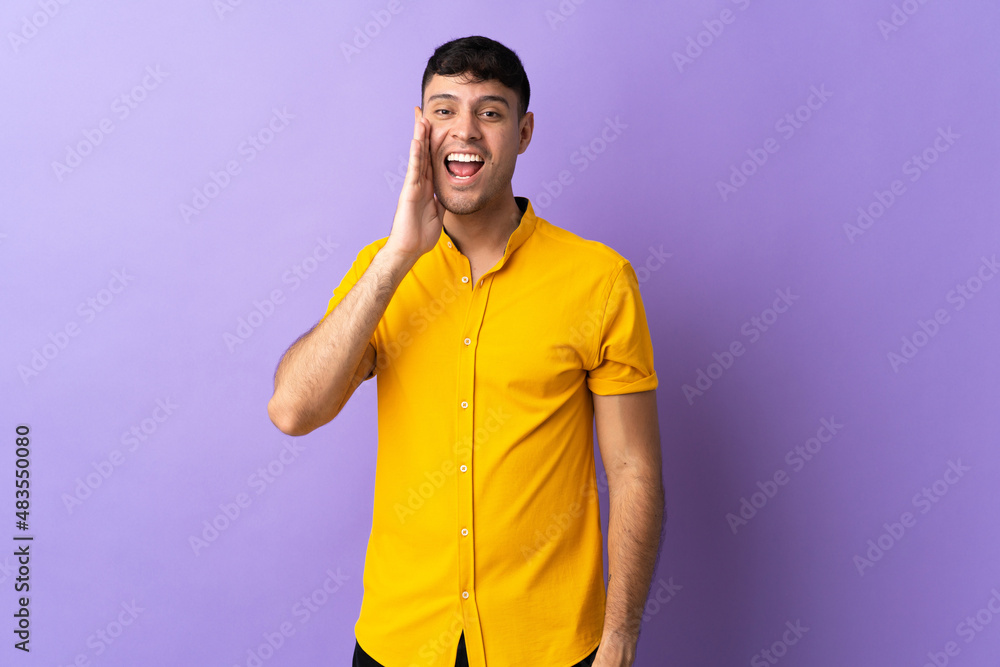 Young Colombian man isolated on purple background shouting with mouth wide open Young Colombian man isolated on purple background shouting with mouth wide open