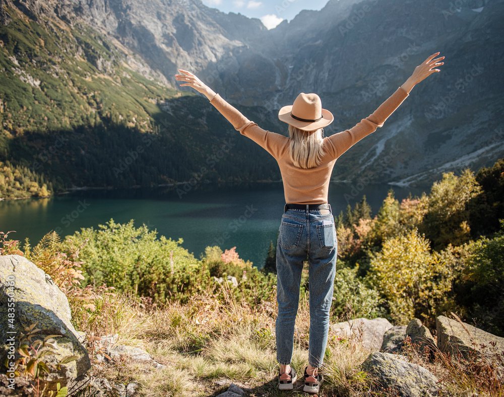 Obraz premium Young tourist woman in a hat with hands up on the top of the mountains