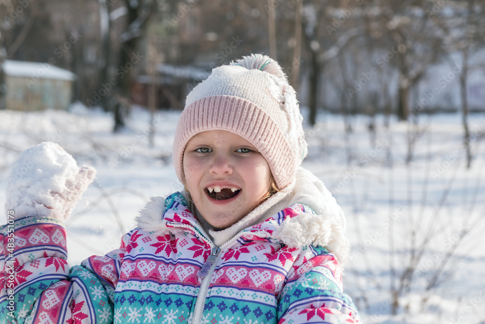 winter portrait of a girl 7-8 years old, smiling, without milk teeth, playing snowballs, winter holidays, the child has fun in a snowy frosty park