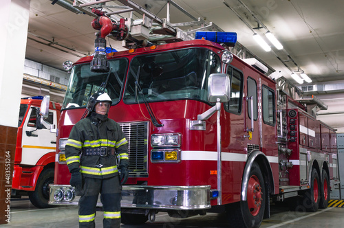 A firefighter in special clothes stands in front of a fire truck. A fire truck at the fire station. Rescue service.