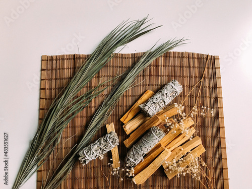 incense on a bamboo brown stand close-up, palo santo from Peru and California white sage, dried flowers around. Art background for text with natural incense and light background blur photo