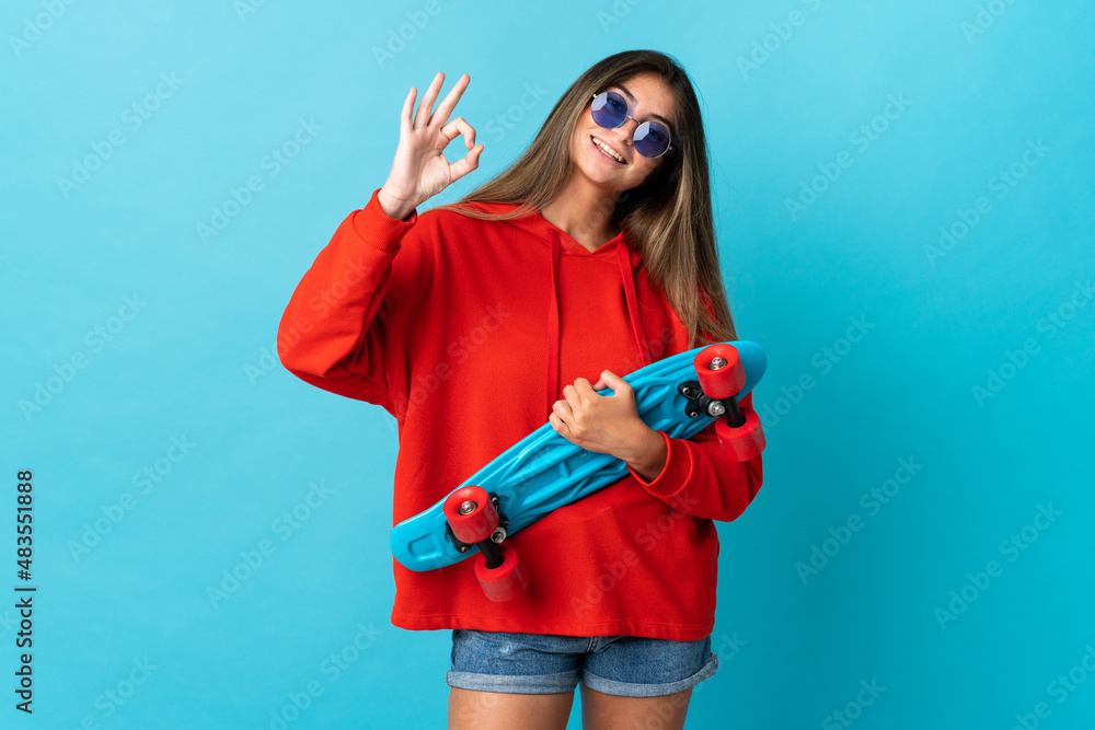 Young caucasian woman isolated on blue background with a skate and doing OK sign Young caucasian woman isolated on blue background with a skate and doing OK sign