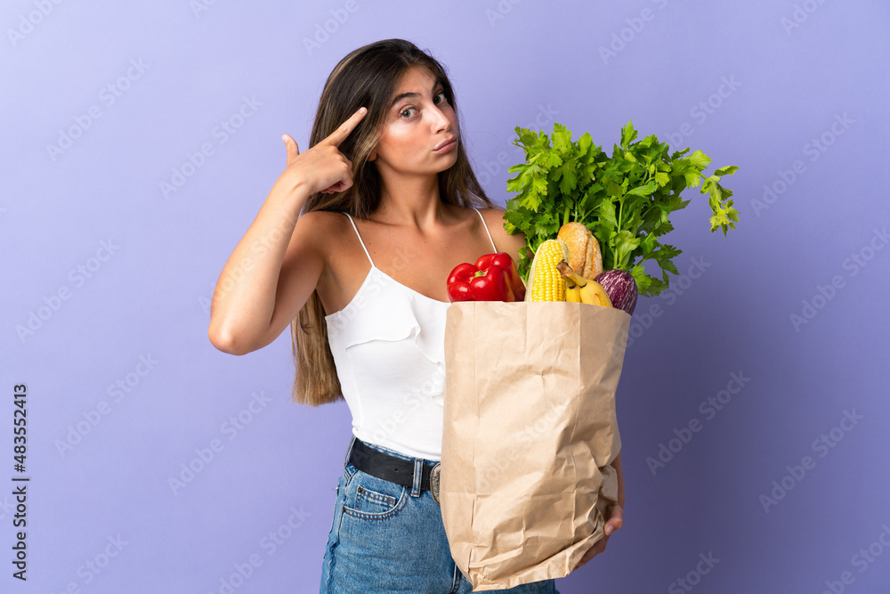 Young woman holding a grocery shopping bag having doubts and thinking Young woman holding a grocery shopping bag having doubts and thinking