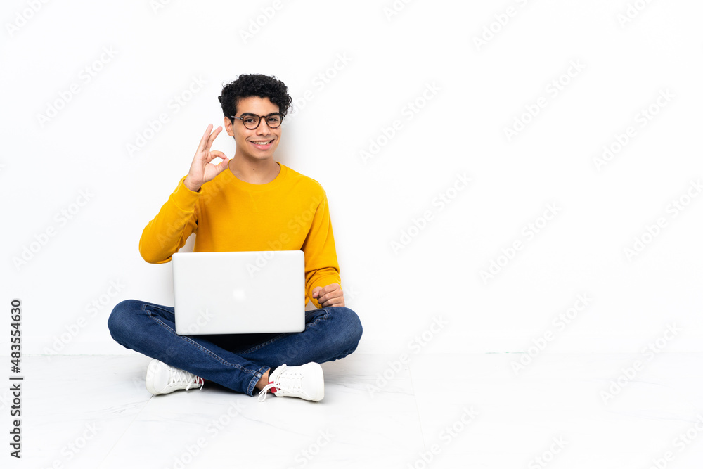 Venezuelan man sitting on the floor with laptop showing ok sign with fingers Venezuelan man sitting on the floor with laptop showing ok sign with fingers