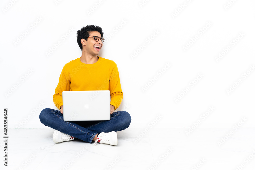 Venezuelan man sitting on the floor with laptop laughing in lateral position Venezuelan man sitting on the floor with laptop laughing in lateral position