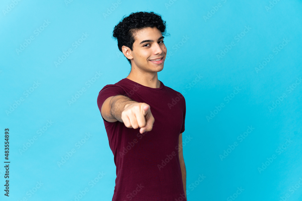 Young Venezuelan man isolated on blue background pointing front with happy expression Young Venezuelan man isolated on blue background pointing front with happy expression