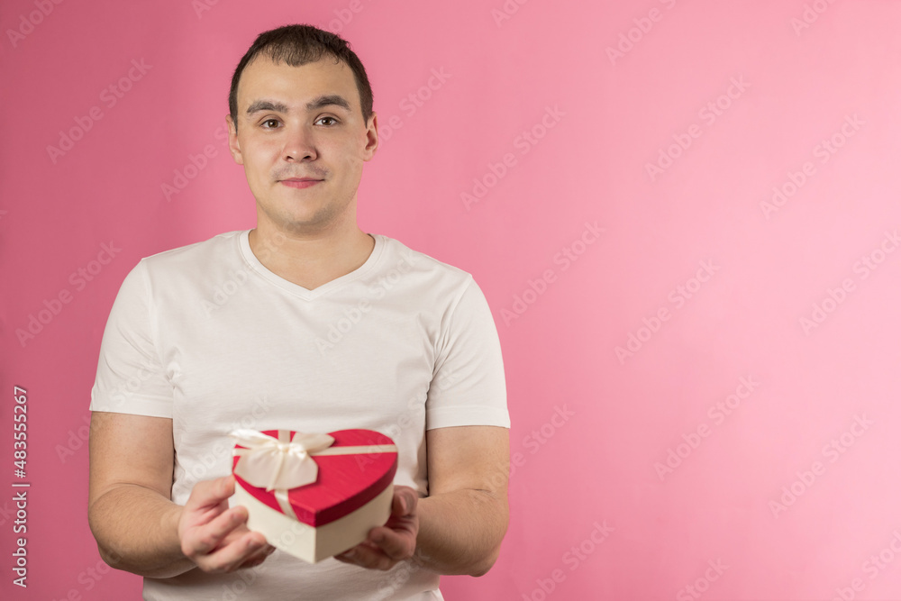 A handsome smiling man gives a gift for Valentine's day, a box of chocolates, a gift box in the shape of a heart, a declaration of love. A man with a gift on a pink background. Advertising banner. A handsome smiling man gives a gift for Valentine's day, a box of chocolates, a gift box in the shape of a heart, a declaration of love. A man with a gift on a pink background. Advertising banner.