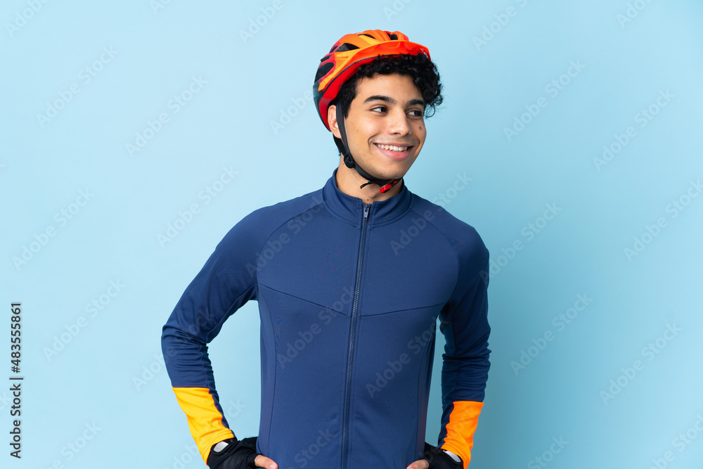 Venezuelan cyclist man isolated on blue background posing with arms at hip and smiling - obrazy, fototapety, plakaty 