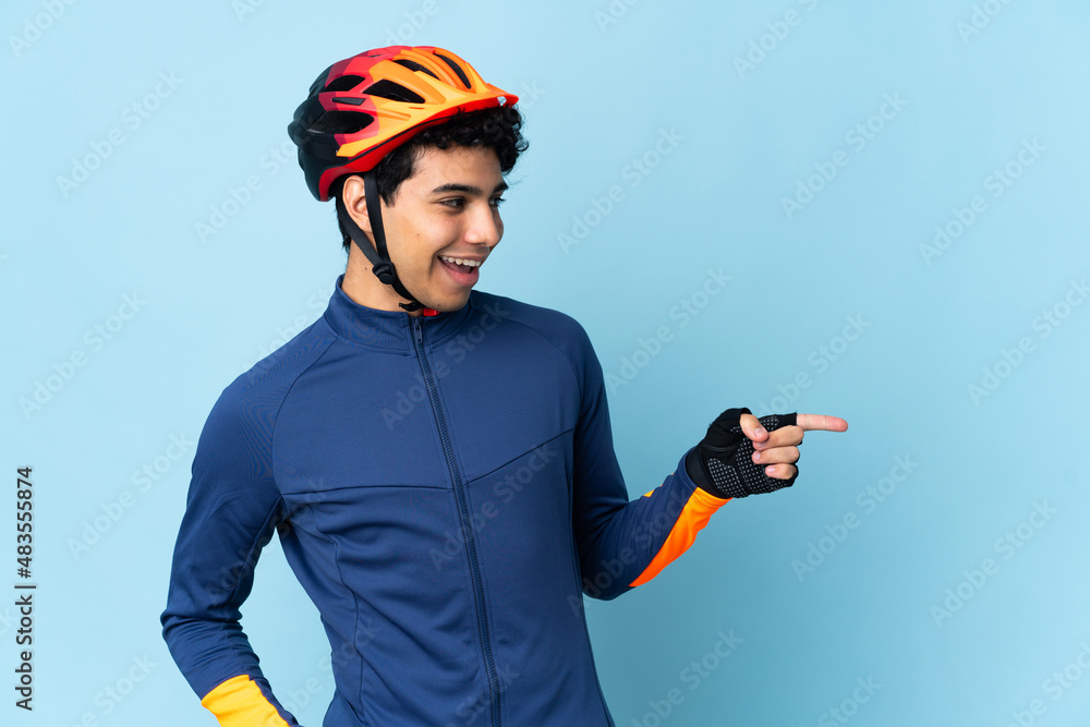 Venezuelan cyclist man isolated on blue background pointing finger to the side and presenting a product - obrazy, fototapety, plakaty 