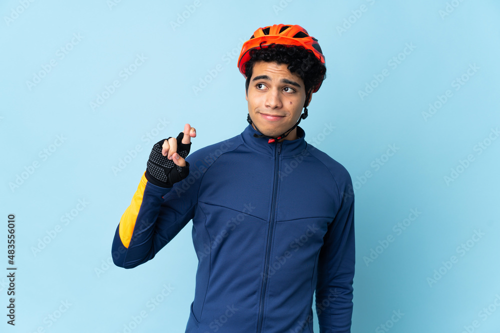 Venezuelan cyclist man isolated on blue background with fingers crossing and wishing the best Venezuelan cyclist man isolated on blue background with fingers crossing and wishing the best
