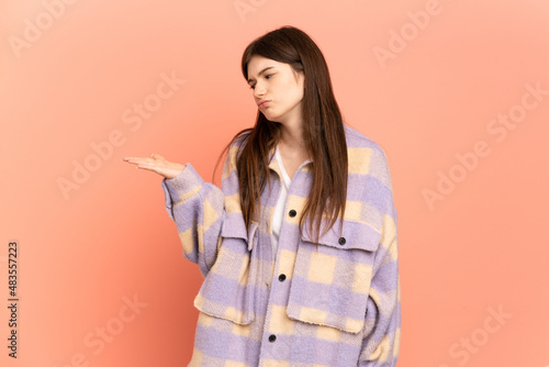 Young Ukrainian girl isolated on pink background holding copyspace with doubts