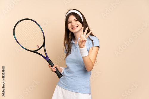 Young Ukrainian girl tennis player over isolated wall happy and counting three with fingers © luismolinero