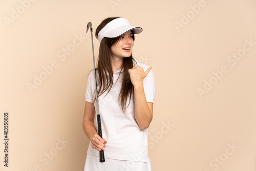 Young Ukrainian golfer girl isolated on beige background pointing to the side to present a product