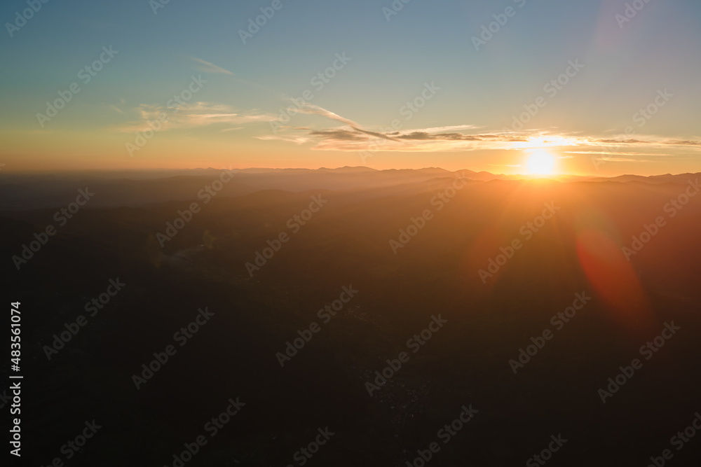 Aerial view of dark mountain hills with bright sunrays of setting sun at sunset. Hazy peaks and misty valleys in evening