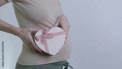 a pregnant woman twirls a pink heart-shaped box with a bow at her stomach. a gift for Valentine's Day or March 8th. video in slow motion.