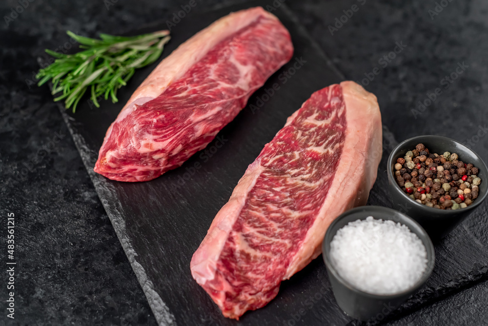 Two raw picanha steaks with spices on a stone background