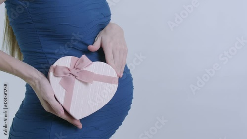 A pregnant woman in a blue dress receives a gift on Valentine's Day or March 8. pink heart-shaped box on a belly background. video in slow motion.