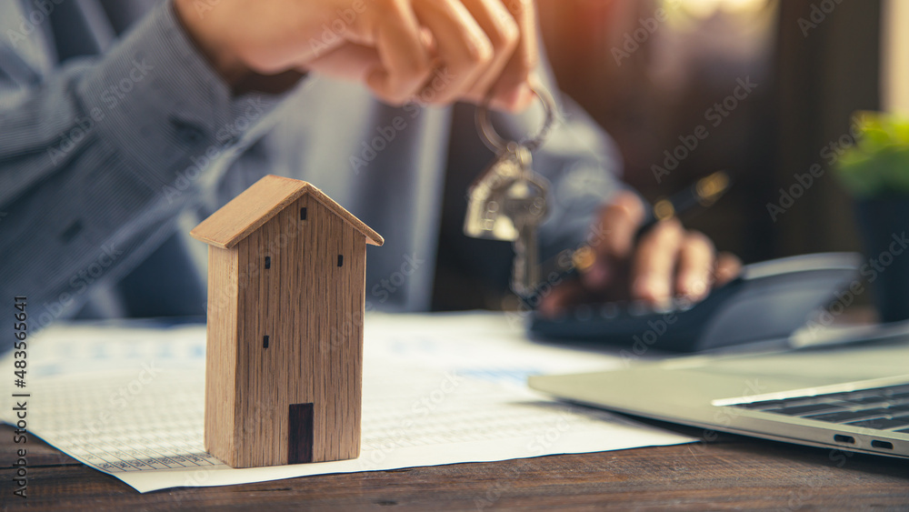 Close up wooden house with hand choose house keys on desk with bank loan documents. Close up wooden house with hand choose house keys on desk with bank loan documents.