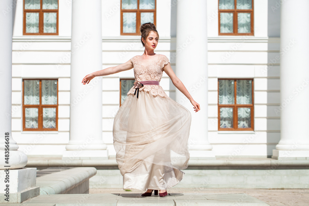 Obraz premium Young woman in a luxurious beige dress posing on the street