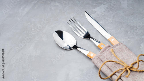 Cutlery on a gray background. Spoon, fork and knife in a linen napkin tied with twine. Table setting. Copy space