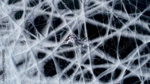Girl and guy tourists are posing on the frozen lake Baikal lying down. Shooting from a drone