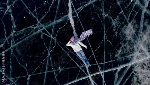 Girl and guy tourists are posing on the frozen lake Baikal lying down. Shooting from a drone