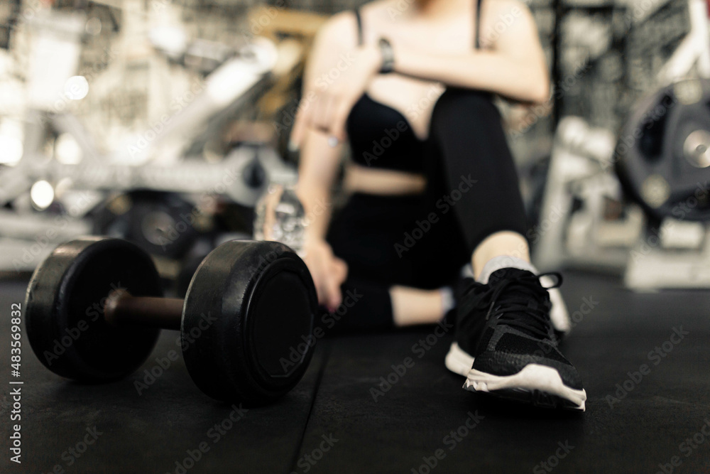 exercise concept The female with dark tone of outfits resting herself on the black carpet floor after playing on the dumbbell beside her exercise concept The female with dark tone of outfits resting herself on the black carpet floor after playing on the dumbbell beside her