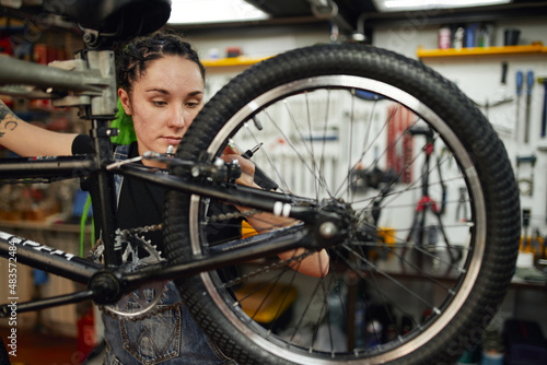 Female mechanic with wrench repairing bike in workshop