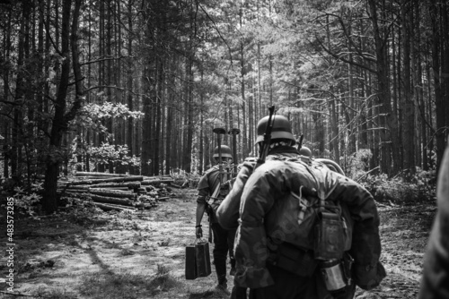 Re-enactors Dressed As German Infantry Soldiers In World War II Marching Walking Along Forest Road In Summer Day. Photo In Black And White Colors.