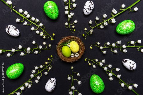 Easter composition. Decorative easter eggs in nest and beautiful white lilies of the valley flowers on black background. Happy Easter concept, greeting card