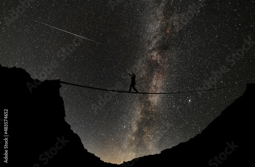 Tightrope walker silhouette in between rocks in the starry night. Mikly way galaxy on the sky. photo