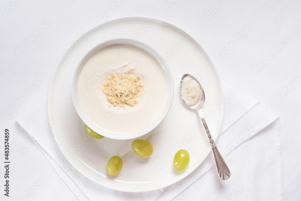 Crema de almendras, sopa fría española. Ajo blanco de Málaga con almendras y uvas en un recipiente blanco sobre una mesa blanca. Vista superior Crema de almendras, sopa fría española. Ajo blanco de Málaga con almendras y uvas en un recipiente blanco sobre una mesa blanca. Vista superior