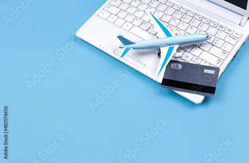 White laptop on blue background. Nearby is a bank card and a miniature airplane