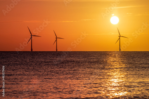 Beautiful orange sunrise with silhouetted offshore wind farm turbines. Clean energy ecotourism and travel image.