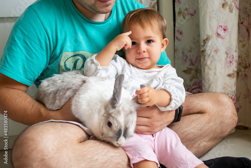 cute little baby play with decorative rabbit in fathers arms at home. domestic animals and children
