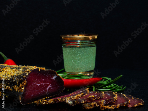 Pieces of basturma with hot pepper and rosemary on black table.