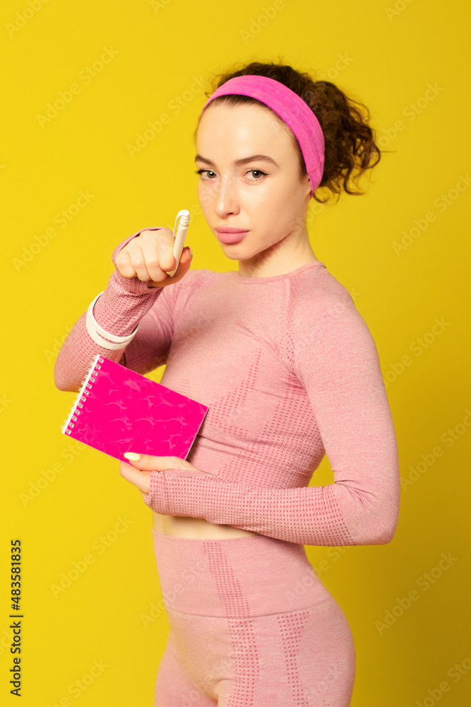 Cute curly-haired young girl holding notepad and pointing pen at camera Cute curly-haired young girl holding notepad and pointing pen at camera