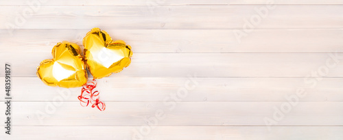 two shiny golden heart-shaped balloon with red ribbon on a white beige and pink wooden background valentines day banner. Valentine's Day banner. The 14th of February banner concept. banner with place