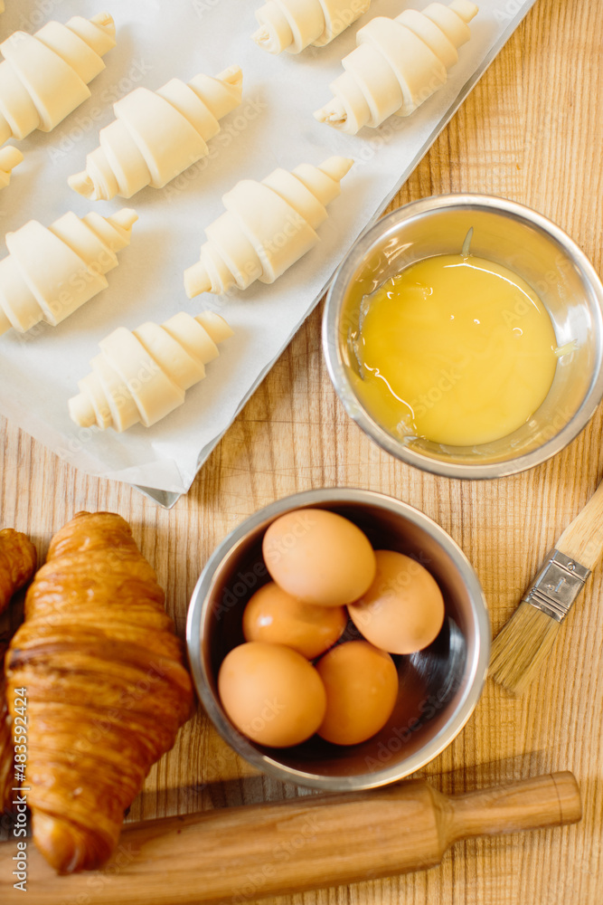 Croissant baking concept. Raw rolled up and freshly baked croissants as well as ingredients lie on the table. Croissant baking concept. Raw rolled up and freshly baked croissants as well as ingredients lie on the table.