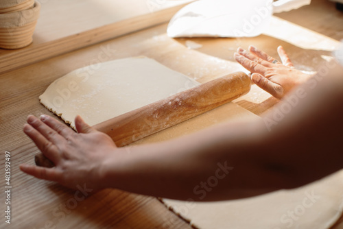 Woman hands rolling out dough in flour with rolling pin in bakery.