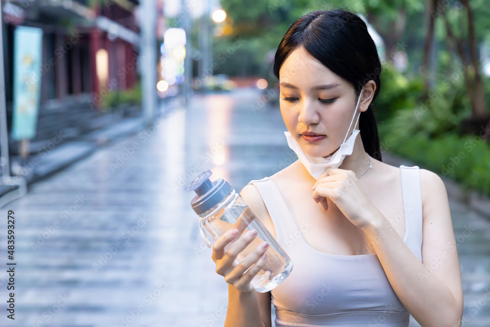 woman runner running with face mask, taking a break to rehydrate with fresh drinking water woman runner running with face mask, taking a break to rehydrate with fresh drinking water