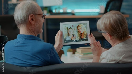 Grandparents talking to family on online conference chat in living room. Senior couple using digital tablet to talk to niece and daughter on remote video teleconference for communication.