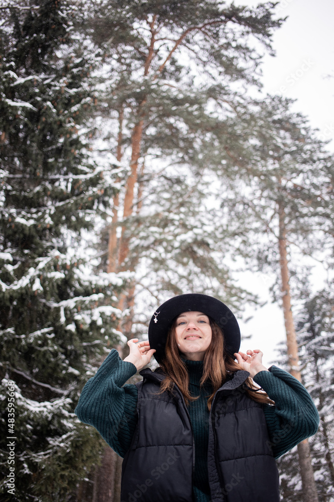 Caucasian young woman in black hat in winter snowy forest.