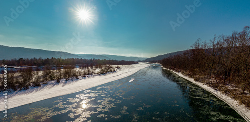 Winter frosty day - panorama. The sun in the blue sky over the mountains and the mountain river on a frosty winter day. Winter panorama of the mountain river Stryi, Carpathians, Ukraine. 