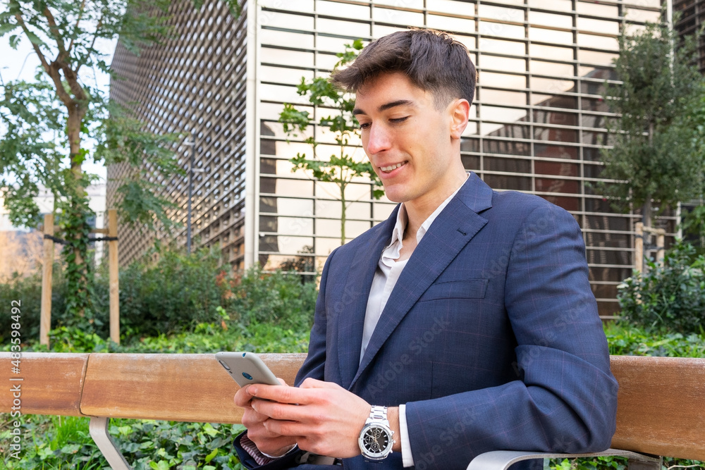 Young entrepreneur sitting on a bench in the financial district and using the mobile. Young business man concept. Young entrepreneur sitting on a bench in the financial district and using the mobile. Young business man concept.