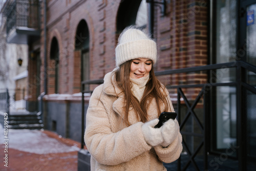 Young woman dressed warmly in winter clothes writing a message on her phone