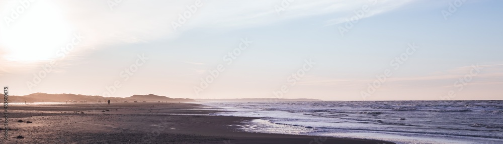 Wide panorama: people walking along the wide Blokhus Strand beach of North Sea. Evening landscape. Nordjylland (North Jutland Region), Denmark